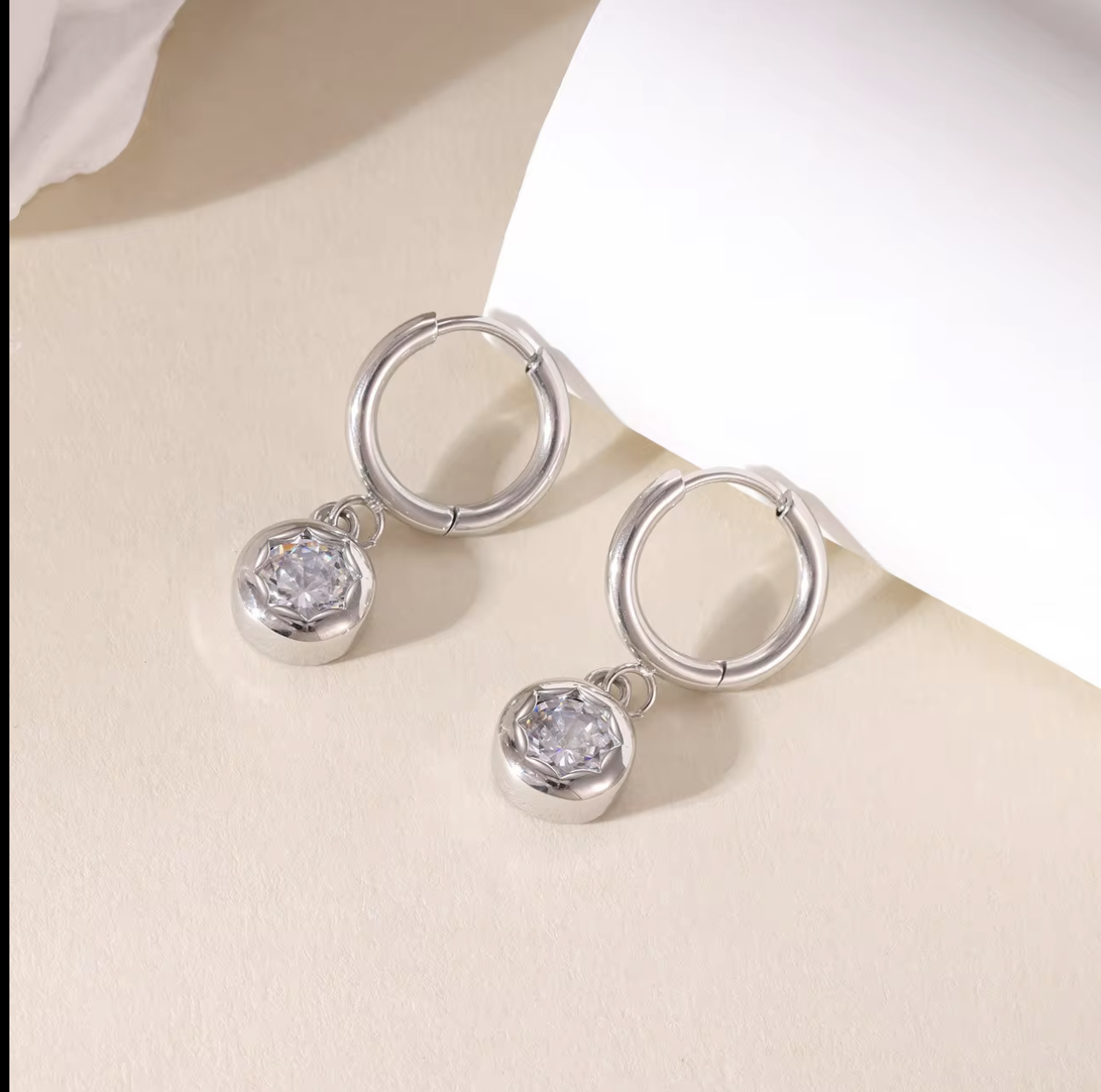 silver hooped earrings with bezel set drop gemstone pictured on a light beige background