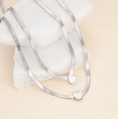 2 silver necklaces photographed on a light beige background