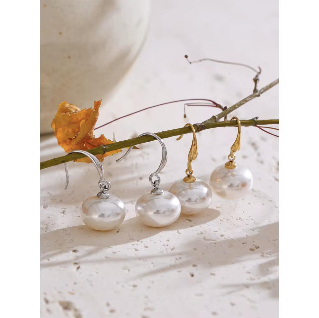 Silver and gold earrings hanging from a branch with a leaf on a light background
