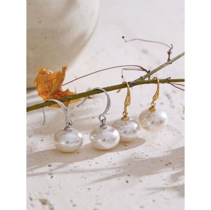 Silver and gold earrings hanging from a branch with a leaf on a light background