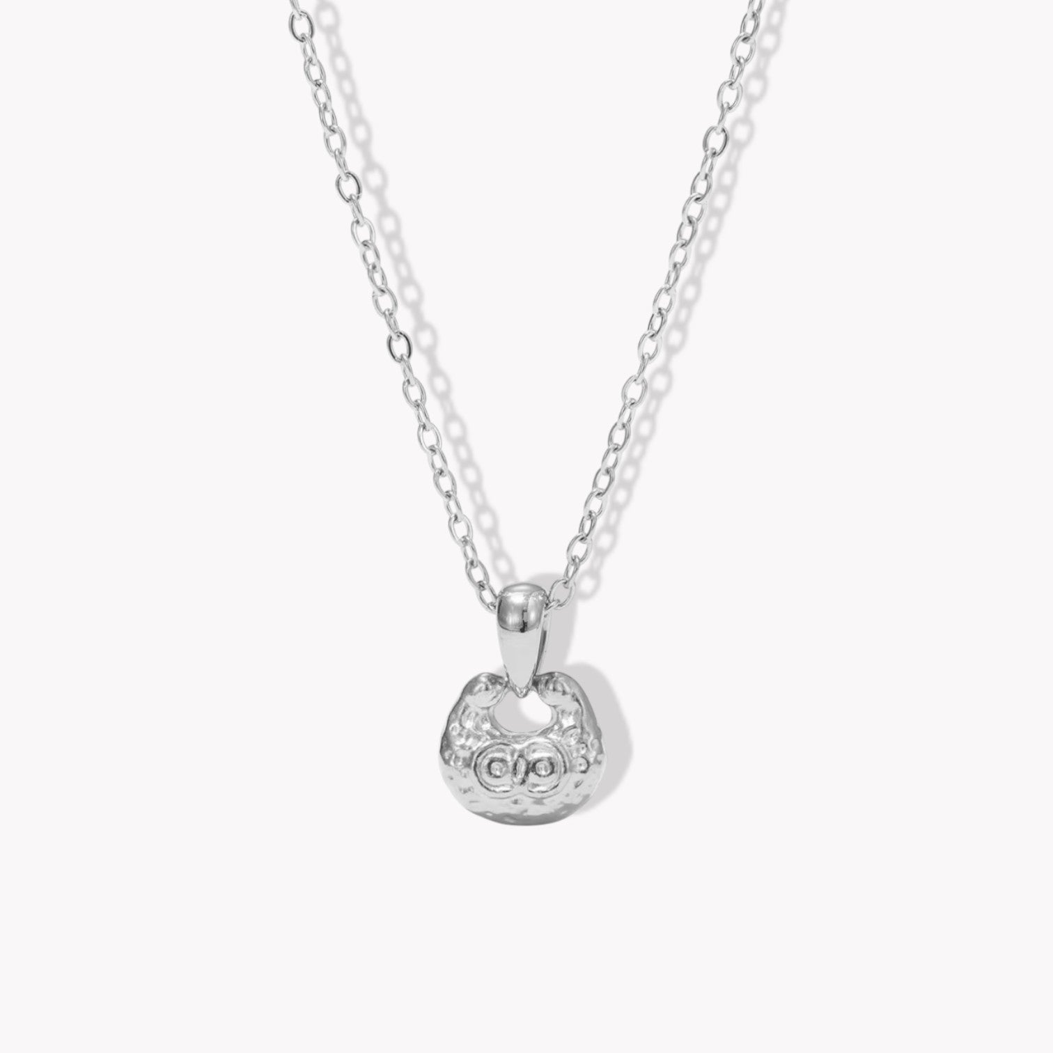 silver necklace featuring small pendant with a textured engave detail pictured on a light background