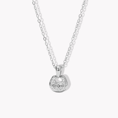 silver necklace featuring small pendant with a textured engave detail pictured on a light background