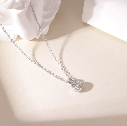 silver necklace featuring small pendant with a textured engave detail pictured on a light background